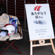 a helmet and racing jacket sit on a chair next to a poster honoring the recently-deceased japanese racing driver Kunimitsu Takahashi